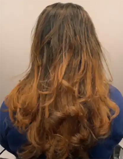 A person with long, wavy brown hair featuring lighter, caramel-coloured highlights, seen from the back.