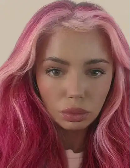 Woman with long, wavy pink hair and full lips looking directly at the camera against a plain background.
