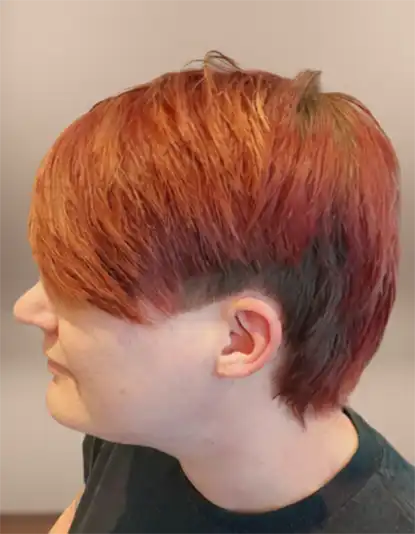 Person with short, straight, red hair featuring an undercut, viewed from the side against a neutral background.