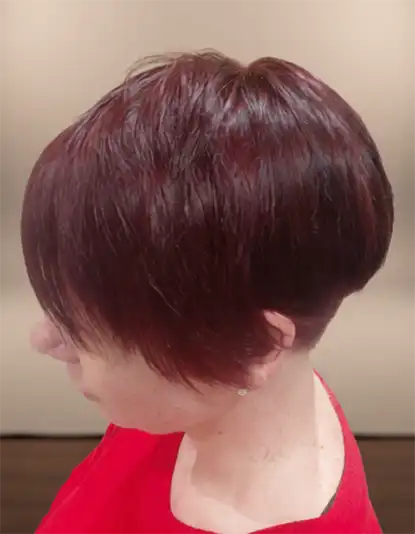 Person with short, dark reddish-brown hair in a sleek pixie cut, wearing a red top, photographed from the side.