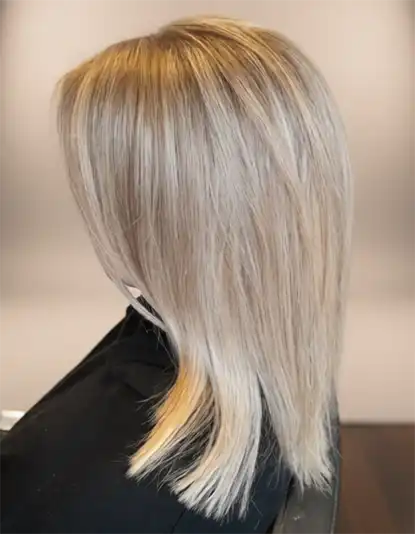 A person with straight, shoulder-length, platinum blonde hair, shown from the side against a neutral background.