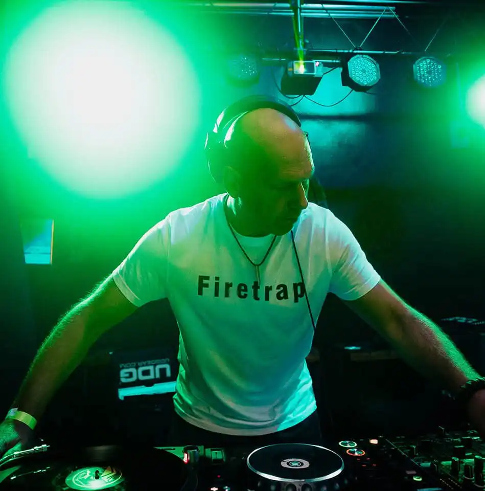 Iain Laidlaw wearing headphones and a Firetrap T-shirt mixes music at a club, surrounded by green stage lights.